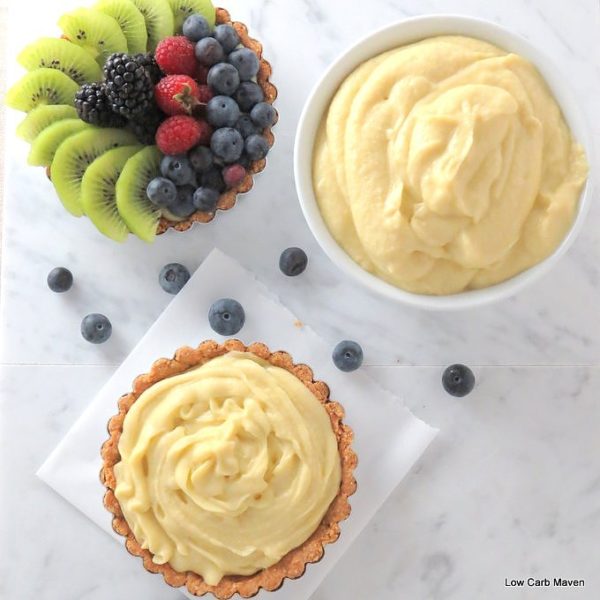 Top-down view of coconut milk pastry cream in a bowl, in a tart shell, and a fresh fruit tart with raspberries, blueberries, blackberries and kiwi.