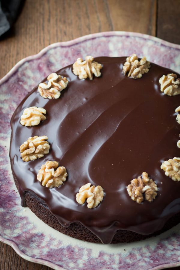 Chocolate cake with ganache decorated with walnut halves on a wavy purple plate.