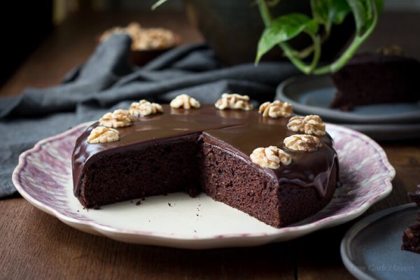 Moist chocolate cake decorated with chocolate ganache and walnuts with a slice missing showing the perfect moist cake texture.