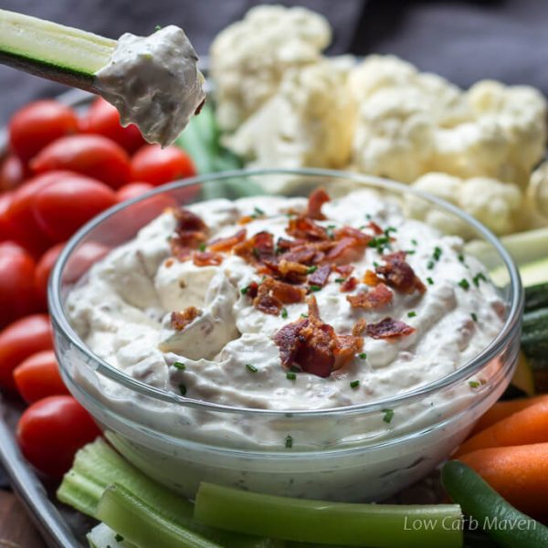Creamy Bacon Horseradish Dip with crumbled bacon on a veggie tray showing a zucchini spear dipped with dip on it.