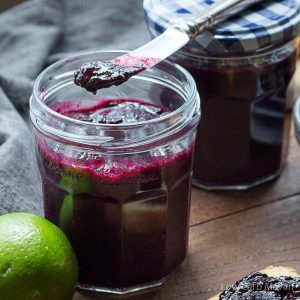 Sugar-free blueberry chia seed jam in a clear glass jar with a lime to the left and a knife with jam over the top of the jar.