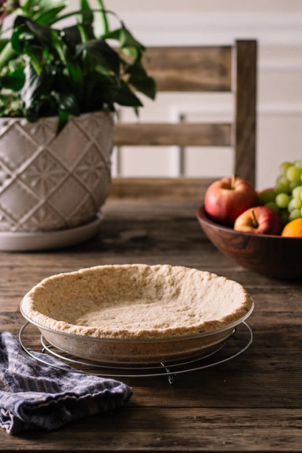 Keto graham cracker crust in pie plate on table with fruit in a bowl.