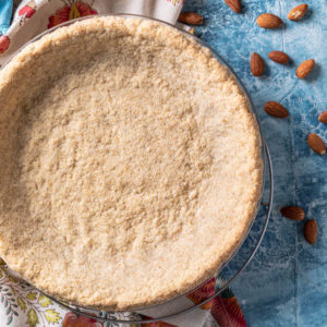 Low carb graham cracker crust (almond flour pie crust) in pie plate on blue background.