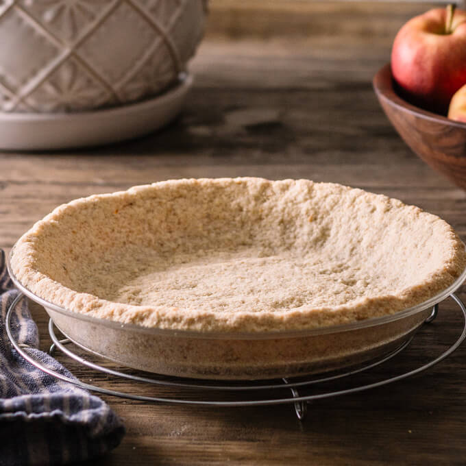 Keto graham cracker crust in pie plate on table with fruit in a bowl.