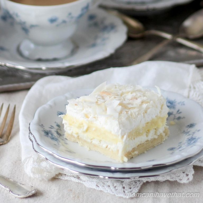 Coconut Cream Layered Dessert (Coconut Cream Delight), 5 layer dessert of a cookie base, cream cheese layer, coconut cream pudding layer, whipped cream and coconut flakes on a blue and white china plate with a lacy napkin beneath.