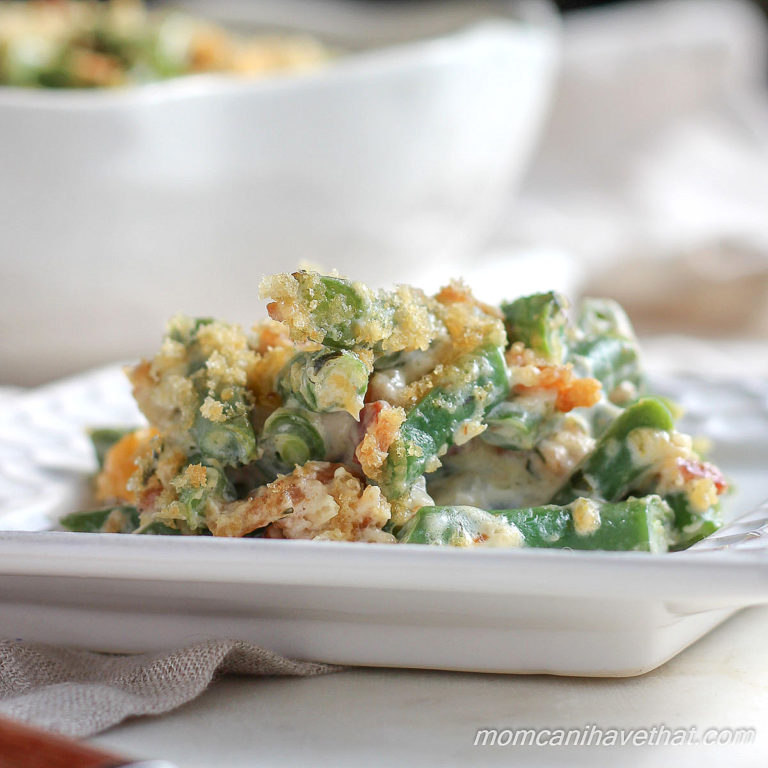 Keto green bean casserole on a white plate showing tender green beans, cheesy sauce, crispy pork rind topping and crispy bacon pieces. 