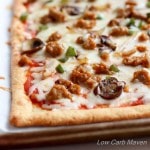 Low Carb Supreme Pizza made with fathead pizza crust on a piece of parchment with cheese, sausage, green onion and mushrooms.