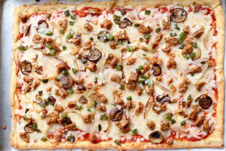 Birdseye view of low carb supreme pizza with fathead pizza crust and sauce, cheese, sausage, green bell pepper, onions and mushrooms on a sheet pan.