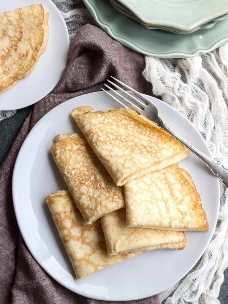 Folded low carb coconut crepes stacked on a plate with a fork. #crepes #lowcarb #keto #coconutflour #sugarfree #glutenfree