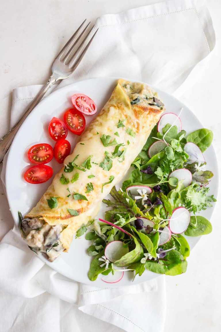 Chicken Florentine Crepes on plate with salad and tomatoes.