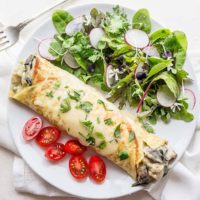 Chicken Florentine Crepes on plate with salad and tomatoes.