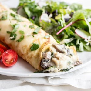 Chicken Florentine Crepes on plate with salad and tomatoes.