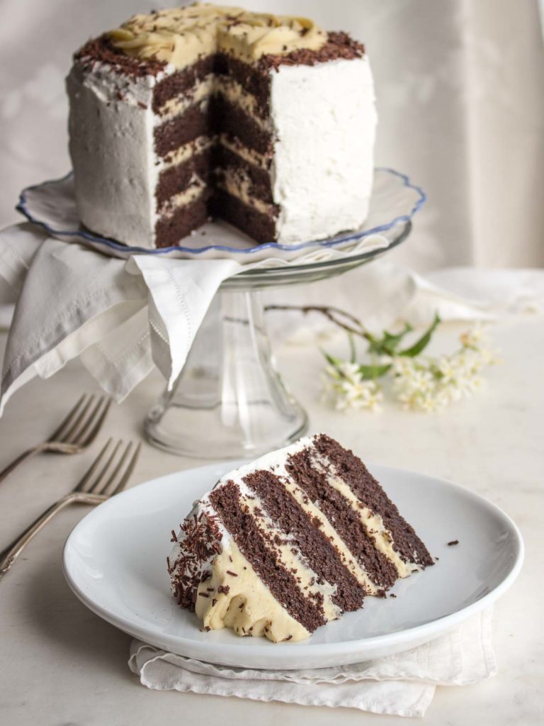 Low carb chocolate layer cake on a cake stand with a slice on a plate.