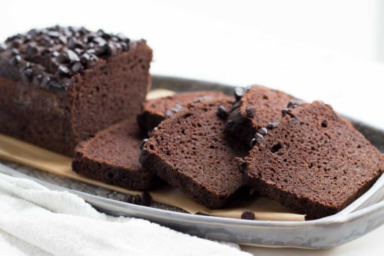 A side view of sliced chocolate pound cake with chocolate chips on a gray oval serving platter with an uncut portion behind the slices on the plate. A white napkin is at the side of the platter.