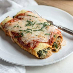 White plate with low carb spinach manicotti and fork.