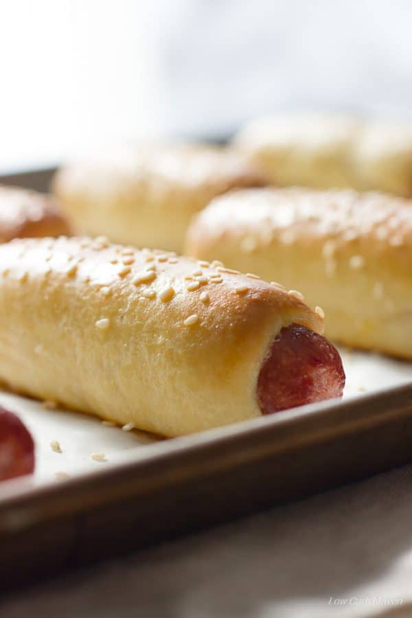 Baked low carb bagel dogs or pretzel dogs with sesame seeds on a cookie sheet.