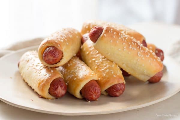 Bagel dogs or pretzel dogs wrapped in fathead pizza crust dough with sesame seeds stacked on an oval platter.