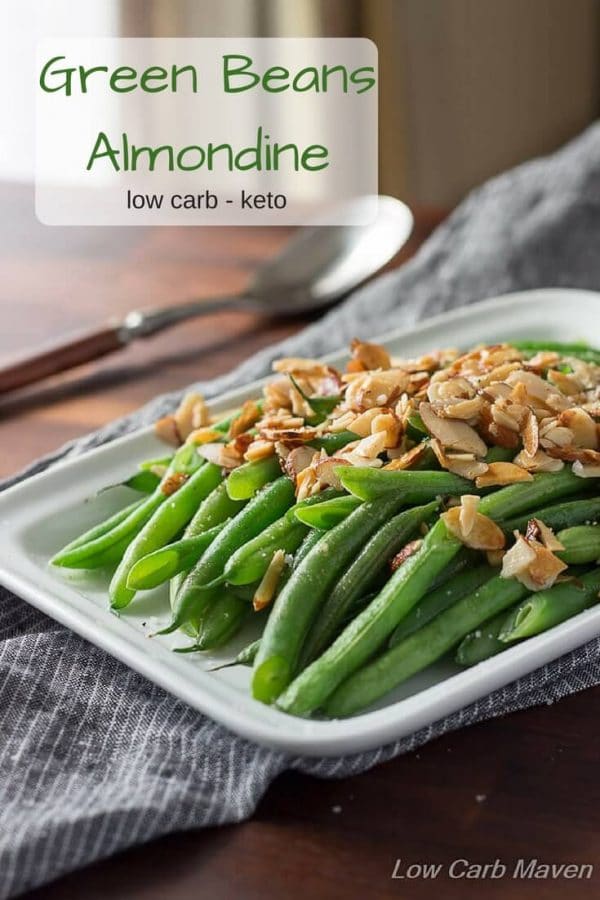 Green beans Almondine on white plate with sliced almonds on top.