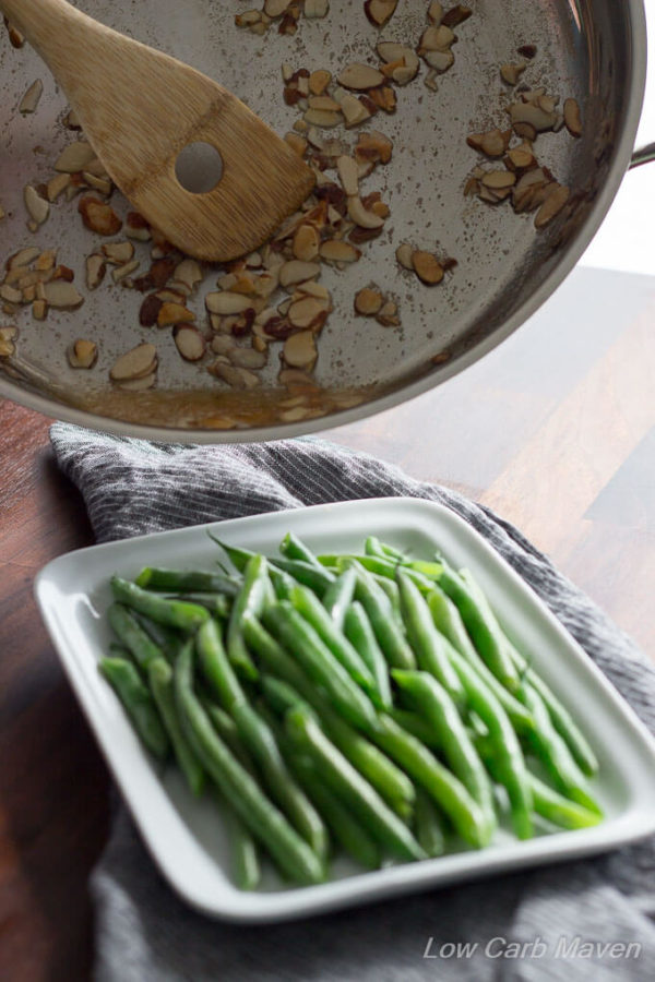 How to make green beans almondine. Pouring melted butter and sliced almonds over cooked green beans. 