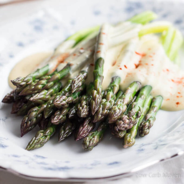 A view from the tip end of steamed asparagus (showing purple and green variations in color) with brown butter Hollandaise and paprika on an oval blue and white floral china plate with a silver edge.