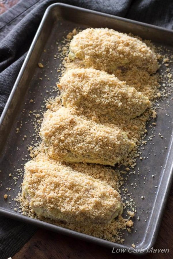 Four chicken breasts in a small rectangular sheet pan sprinkled with a low carb crumb coating of pork rinds and Parmesan cheese.
