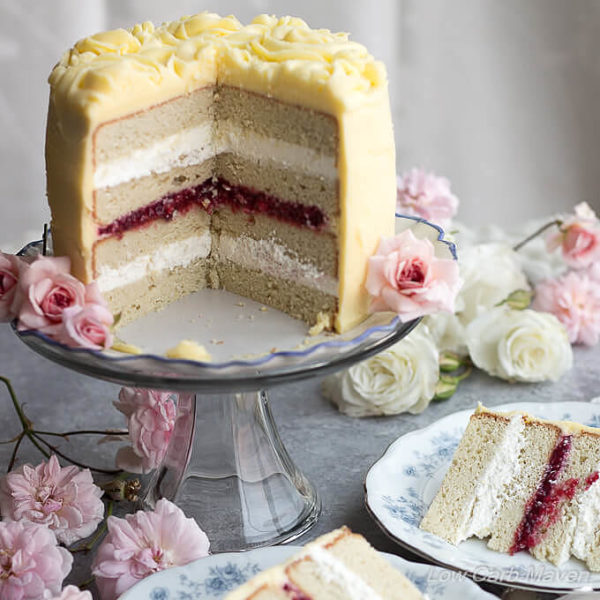 Cut white layer cake on a pedestal decorated with yellow frosting and rosettes on a table decorated with white and pink roses and blue and white china dishes.