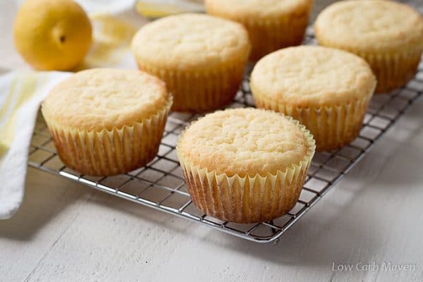 Six sugar-free lemon cupcakes on a cooling wrack with a yellow striped tea towel and a lemon.
