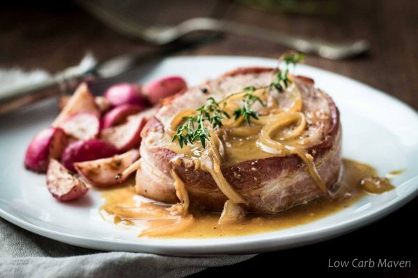 Bacon wrapped pork chop with onions and glossy pan sauce topped with thyme and served with sauteed radishes.