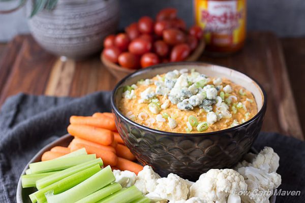 Buffalo Chicken dip topped with scallions and blue cheese in a bowl with raw vegetables.