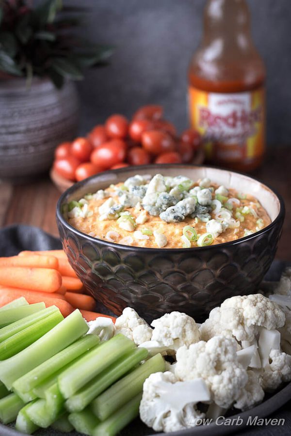 Buffalo Chicken dip topped with scallions and blue cheese in a bowl with raw vegetables and Frank's Red Hot Buffalo Sauce.