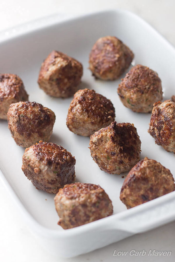 Pan fried Italian meatballs lined up in rows in a white porcelain baking dish.