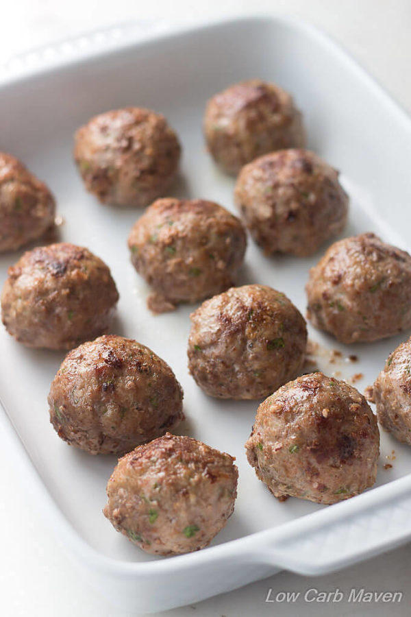 Round, baked meatballs lined up rows in a white rectangular porcelain dish.