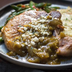 Mexicaans karbonade recept met chili verde saus en cotija kaas geserveerd met mexicaanse sperziebonen en tomaten en cheesy bloemkool puree op een donkere handgemaakte plaat.