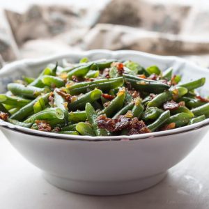 Sweet and sour German green beans with bacon, onions and whole mustard seeds in a white bowl.
