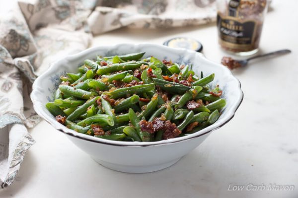 Sweet and sour German green beans with bacon, onions and whole mustard seeds in a white bowl.