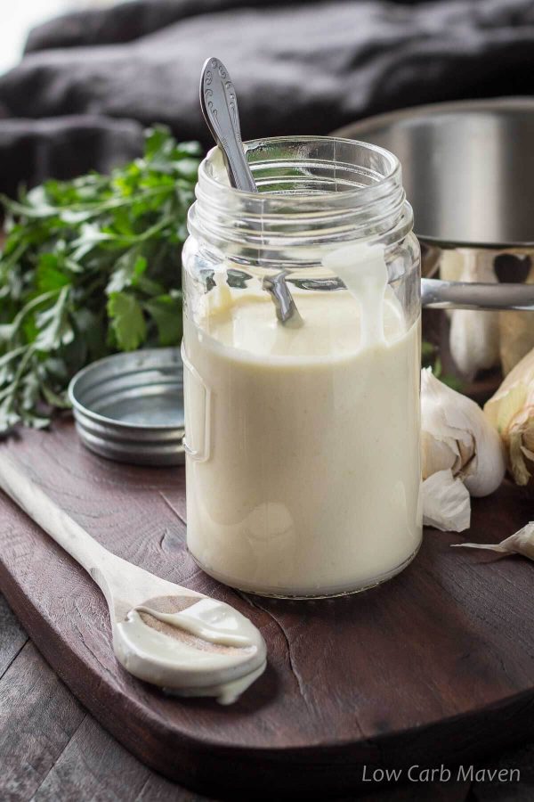Creamy keto Alfredo sauce in a jar with wooden spoon beside showing a creamy sauce texture. 