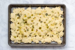 Low carb focaccia dough topped with olive oil dipping sauce in a sheet pan before baking.