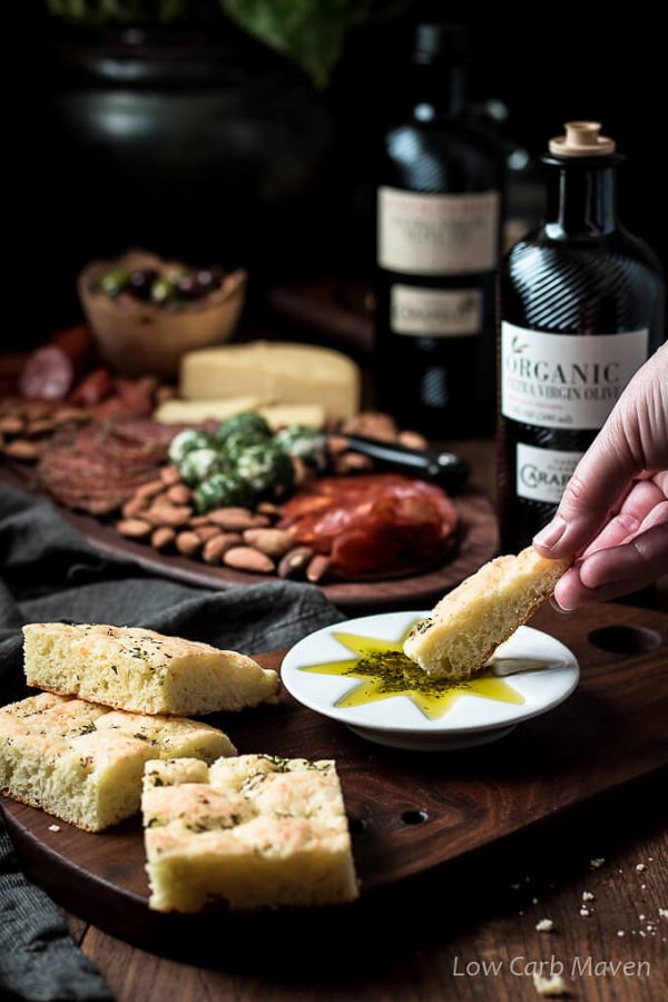 Gluten free low carb Focaccia with olive oil dipping sauce on a cutting board with Carapellli Olive Oil.