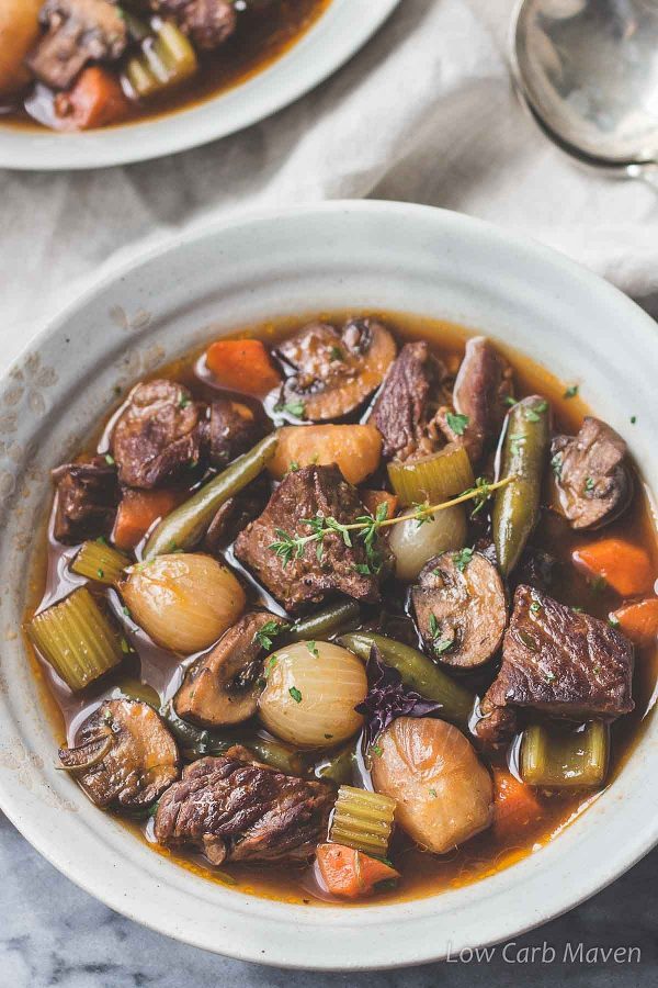 Keto beef stew with chunks of beef, pearl onions, carrot, celery, mushrooms, green beans and fresh thyme in a bowl.