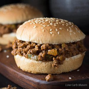 homemade sloppy joes recipe with onions and bell peppers in the sauce on sesame seed buns on a cutting board.