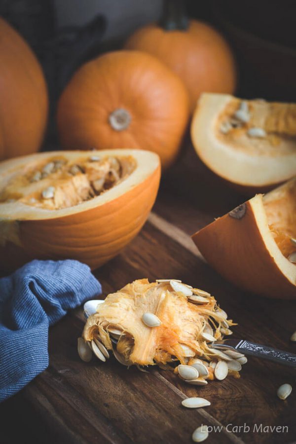 Cut and whole pumpkins on a cutting board with a blue napkin and freshly scooped pumpkin seeds.