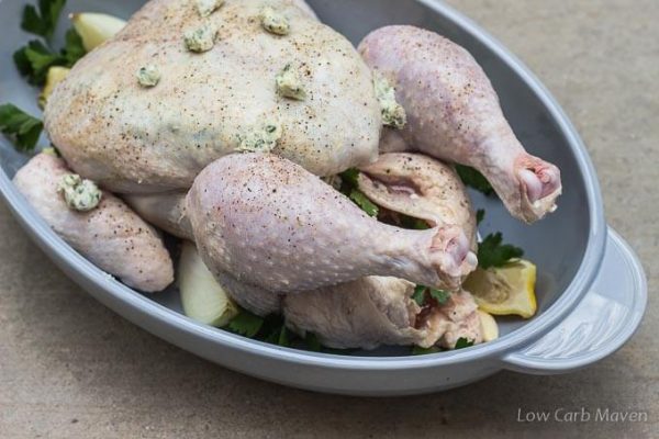 Simple roast chicken with herb butter trussed in a roaster with vegetables.