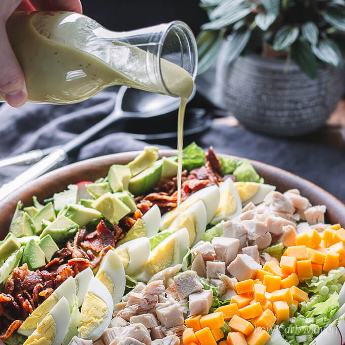 Chicken Cobb salad with toppings in a wooden salad bowl drizzled with Cobb salad dressing.