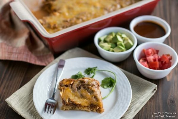  A serving of Mexican chicken casserole on a plate with a fork and cilantro, avocado, and tomato.