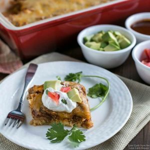 A serving of Mexican chicken casserole with sour cream, avocado, tomato and cilantro on a plate with a fork.