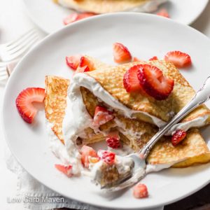 Folded coconut flour crepes with strawberries and whipped cream on a plate with fork.