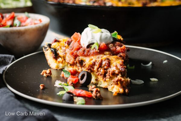 Slice of keto tamale pie on a black plate with salsa, cream cheese and black olives.