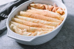 Chicken enchiladas rolled in crepes in a white baking dish.