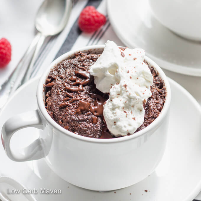 Keto chocolate cake in a cup with melted chocolate, whipped cream, and raspberries.