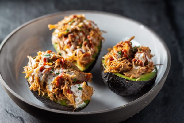 Stuffed avocados or avocado boats with pulled pork, cheese, and BBQ sauce in a bowl.